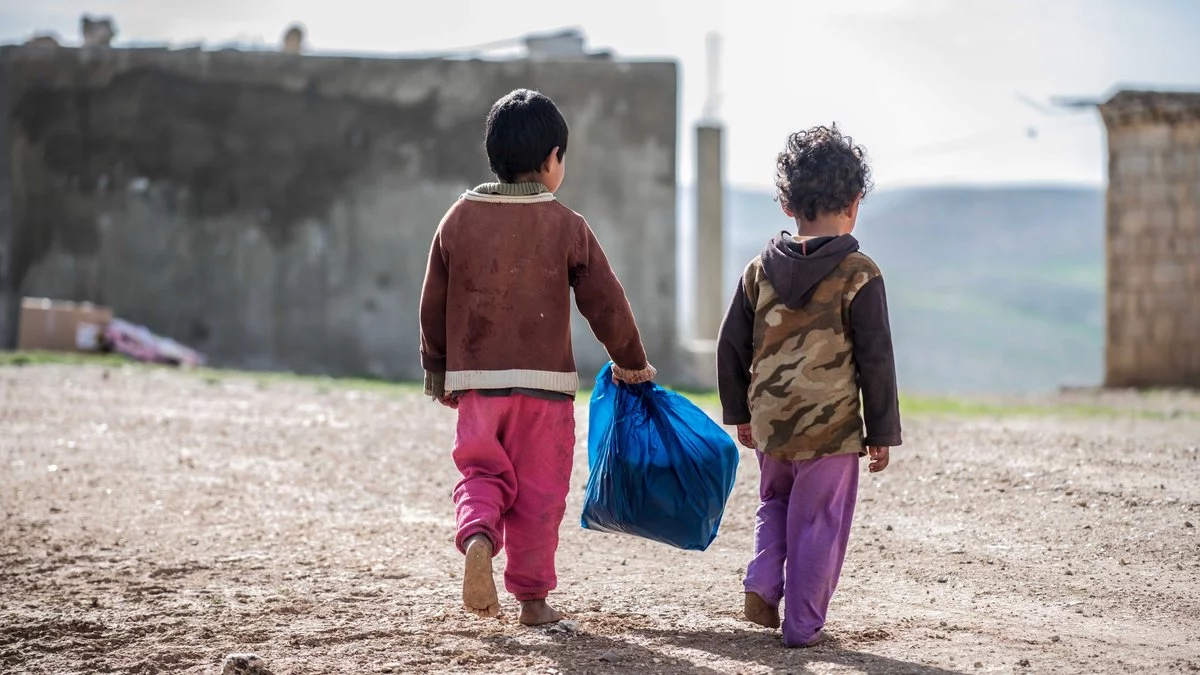 Two children walking together while carrying a blue bag